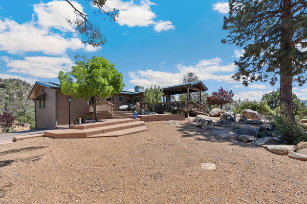 There is a quaint house that is beautifully positioned on top of a dirt hill, which is surrounded by a variety of lush green trees