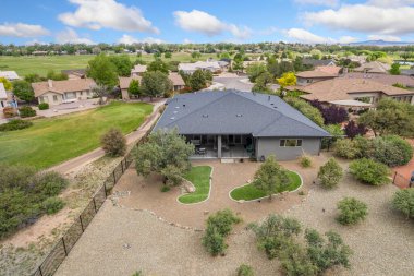 Bu resim, bereketli ağaçlar ve canlı otlar tarafından kucaklanan huzurlu bir yerleşim alanına yerleştirilmiş resimli bir evin havadan görüntüsünü sergiliyor.