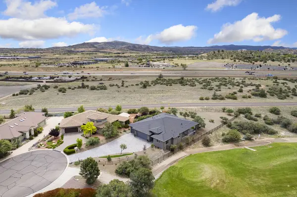 Yüksek perspektiften bakıldığında, havadan bakıldığında arka plandaki görkemli dağlar tarafından çerçevelenmiş engin bir golf sahasının yanında güzel bir ev sergileniyor.