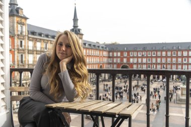 Bir kadın, güzel bir balkonda huzurlu bir şekilde oturuyor, nefes kesici bir şehir manzarasına bakıyor ve eğleniyor.