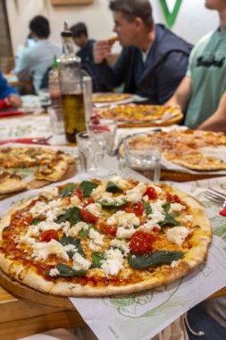 Farklı bireylerden oluşan bir grup bir masanın etrafında toplanmış lezzetli pizza dilimlerinin tadını çıkarıyor, harika anlar paylaşıyor ve gülüyorlar.