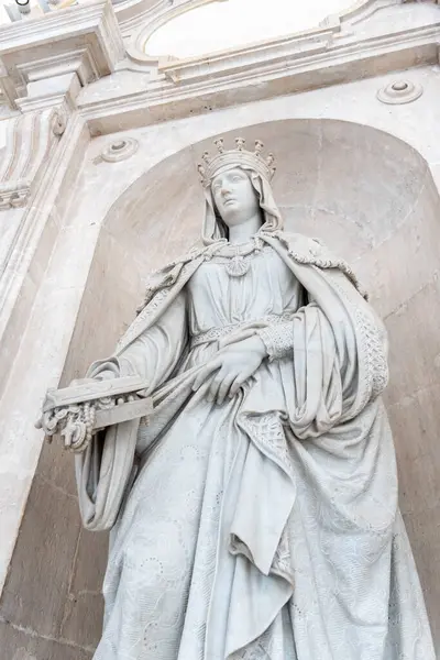 Akan beyaz bir elbise giymiş güzel bir kadın heykeli zarif bir şekilde muhteşem bir binanın önünde duruyor.