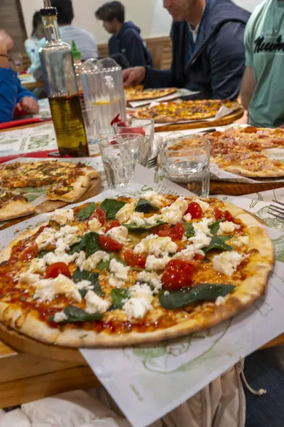 Farklı bireylerden oluşan bir grup bir masanın etrafında toplanmış lezzetli pizza dilimlerinin tadını çıkarıyor, harika anlar paylaşıyor ve gülüyorlar.