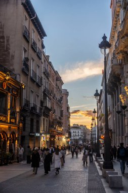 Madrid, İspanya - 1 Mart 2024: Oldukça bulanık bir resim, güzel bir gün batımı anında kalabalık bir şehir caddesinde sakin bir şekilde yürüyen birkaç kişiyi görüntüler.