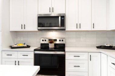 Beyaz dolaplarla donatılmış modern bir mutfak, parlak bir siyah soba, ve pişirme verimliliğini arttıran işlevsel bir mikrodalga.