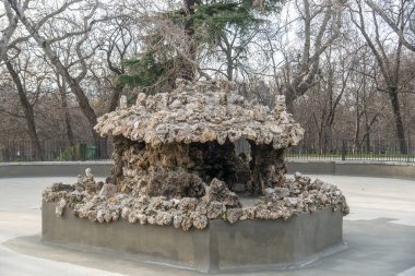 Güzel bir parkın ortasında, arkasında durgun bir zemin oluşturan uzun, yeşil ağaçlarla çevrili çarpıcı bir heykel duruyor.