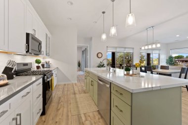 Zarif beyaz dolaplara, paslanmaz çelik aletlere ve işlevselliği artıran etkileyici derecede büyük bir adaya sahip modern bir mutfak.