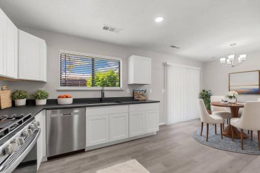 Modern beyaz dolaplar, paslanmaz çelik aletler, geniş bir soba ve bulaşık yıkamak için temiz bir lavabo içeren parlak ve şık bir mutfak.