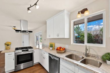 Zarif beyaz dolaplar, modern paslanmaz çelik aletler, lavabo ve tüm yemek ihtiyaçlarınız için bir soba içeren güzel tasarlanmış bir mutfak.