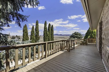 Uçsuz bucaksız ahşap bir güverte. Uzaktaki ağaçların ve görkemli dağların nefes kesici manzarasını sunar.