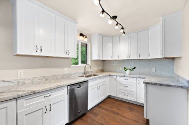 Zarif beyaz dolaplar, çarpıcı granit tezgahlar ve işlevselliği artıran modern paslanmaz çelik aletler içeren güzel tasarlanmış bir mutfak.