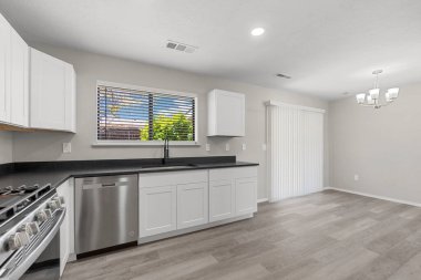 Parlayan beyaz dolaplar, modern bir soba, derin bir lavabo ve geniş bir pencerenin yer aldığı geniş, boş bir mutfak.