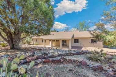 Önünde zarif bir şekilde yerleştirilmiş yemyeşil ağacı olan büyüleyici beyaz bir ev var. Resimli bir manzara yaratıyor.