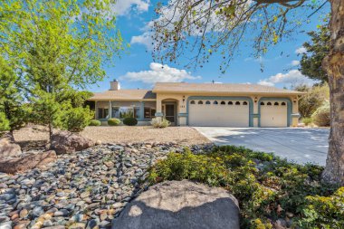 Önünde zarif bir şekilde yerleştirilmiş yemyeşil ağacı olan büyüleyici beyaz bir ev var. Resimli bir manzara yaratıyor.