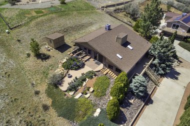 Ağaçlarla çevrili ferah bir evi gösteren bir hava manzarası, iyi korunmuş bir garaj yolunun yanında.