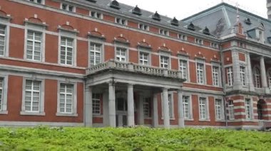 Zarif bir balkonu ve bir sürü penceresi olan büyüleyici bir kırmızı tuğla bina. Bir kadın dolaşır, sakin sahneyi güzelleştirir.