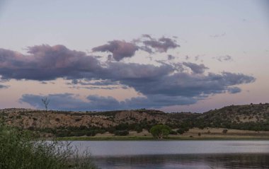 Güzel gölün sakin yüzeyinde, kabarık bulutlar tembelce gökyüzünde sürükleniyor, çarpıcı bir doğal manzara yaratıyor.