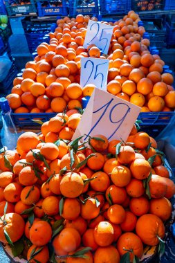 Üzerinde 19 yazan bir tabela olan bir yığın portakal. Portakallar üst üste yığılmış ve mavi bir kabın içindeler.