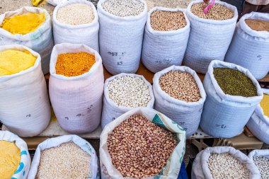 Fasulye, pirinç ve mısır da dahil olmak üzere çeşitli renkli yiyecek torbaları. Çantalar birbiri üzerine istiflenerek renkli ve çeşitli bir ekran oluşturuyor.