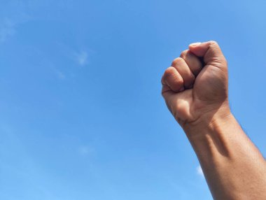 Close-up of hand punching the air against a bright blue sky. success and winner concept. Human hand fist into blue sky. clipart