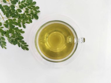 Kaynamış moringa beyaz arka planda üst açılı cam içinde su bırakır. Sağlıklı içki yaşam tarzı 
