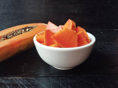 Kâsede taze papaya meyvesi dilimleri ve siyah ahşap masada papaya meyvesinin yarısı. 