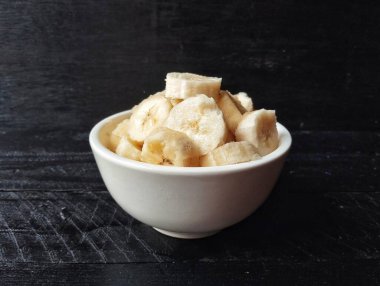 Siyah ahşap masa arkasında kasede taze muz dilimleri. 