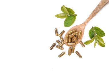 Alternatif tıp bitkisel kapsülleri tahta kaşıkta yeşil yapraklı beyaz arka planda, kopyalama alanı 