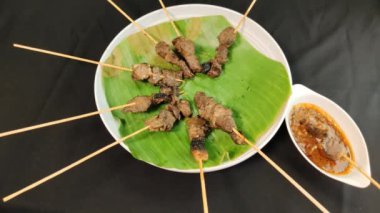 Soto çorbasına batırırken bir şişe satayayı fıstık sosuna batırmak.