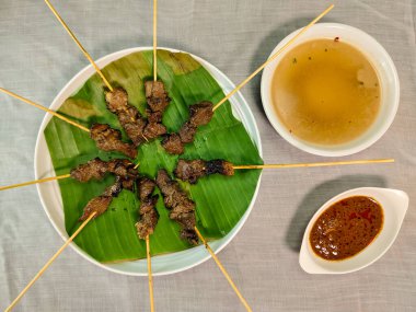 Matang satay or Sate Matang with complementary seasoning of peanut sauce and soup stock on white table clipart