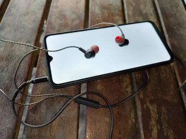 Tahta bir bankta akıllı bir telefon ve kulaklık.