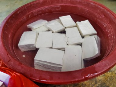 Plastik bir kapta suyla doldurulmuş bir avuç çiğ tofu parçasına yakın çekim yapın.