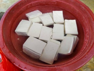 Plastik bir kapta suyla doldurulmuş bir avuç çiğ tofu parçasına yakın çekim yapın.