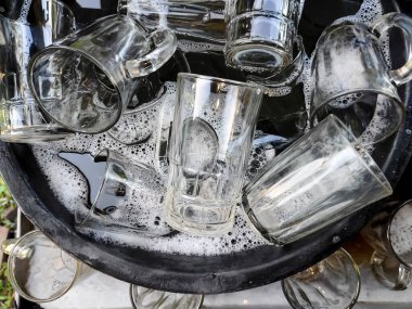 Bir kova sabunlu suyun içinde bir yığın bardak.