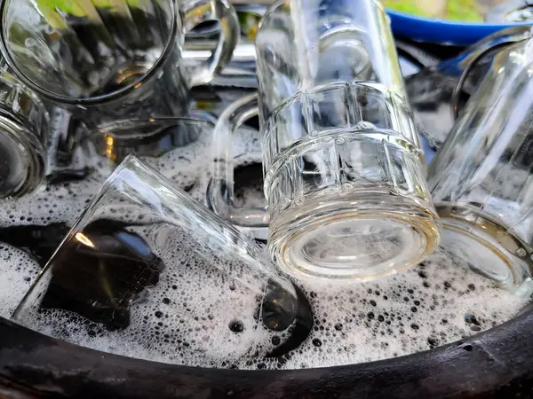 Bir kova sabunlu suyun içinde bir yığın bardak.