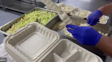 Yemek kutularına pirinç ve yiyecek servisi yapan kişi, dağıtım veya teslimat için gıda paketleme sürecini gösteriyor. Yemek servisi, yemek hazırlama, yemek teslimatı gibi konular için uygun