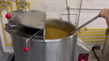 Fasulyelerle dolu büyük bir endüstriyel düdüklü tencere. İçinde bir kepçeyle, hareketli bir ticari mutfakta çorba karıştıran biri var. Geniş çaplı gıda hazırlığı için mükemmel.