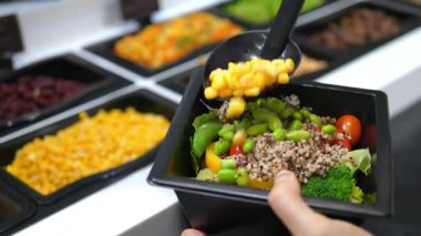 Canlı bir salata barındaki kinoa salatasına mısır ekleyen bir elin yakın çekimi..