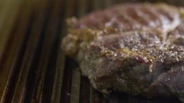 Sıcak ızgarada cızırdayan lezzetli bir bifteğin yakın çekimi görünür duman ve ızgara izleriyle.