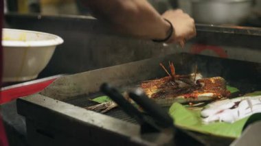 Asya 'da bir sokak yemekhanesinde muz yaprağında balık ızgara yapan bir şefin yakın plan fotoğrafı..