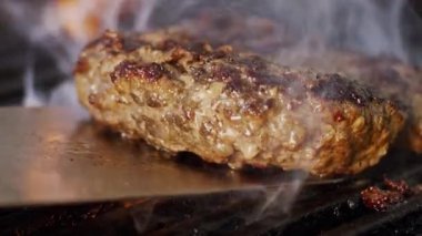 Sıcak metal bir spatula üzerinde ızgara yapılan sulu bir sığır burger köftesinin yakın plan çekimi..
