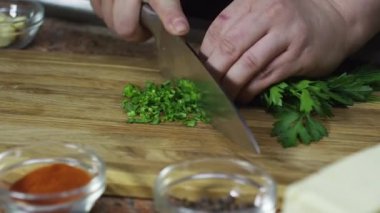 Yeni maydanoz doğrayan bir şefin elleri ve ahşap kesim tahtasının üzerinde soğan soğanları..