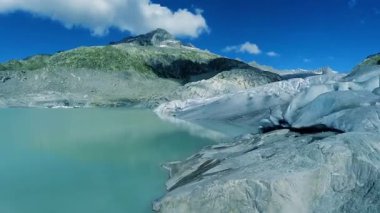 Görkemli dağlarla çevrili Alplerde yuva yapmış turkuaz bir buzul gölü ve bir buzulun çarpıcı panoramik görüntüsü..