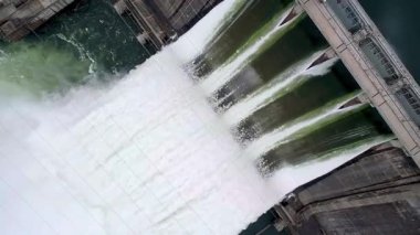 Aerial View of Dam Overflowing with Powerful Water Discharge. A dramatic aerial shot captures a massive dam releasing powerful streams of water through its gates. 