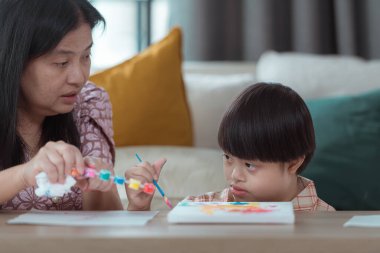 Annesiyle birlikte evin oturma odasında resim yapan özel bir çocuk.