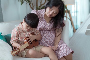 Annesiyle birlikte özel bir çocuk evin oturma odasında ukulele çalıyor.