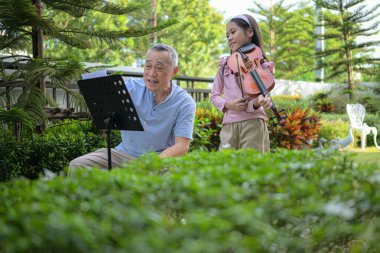 Bir kız kemancı ve dedesi evdeki bahçede birlikte müzik çalıyorlar.