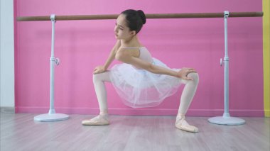 Bir kız bale öğrencisi pembe ve beyaz bir geçmişle evde bale yapıyor.