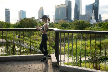 Genç bir kadın, sosyal medyaya bağlanmak ve rahatlatıcı müzik dinlemek için akıllı telefon kullanarak egzersiz yaparken ara veriyor.