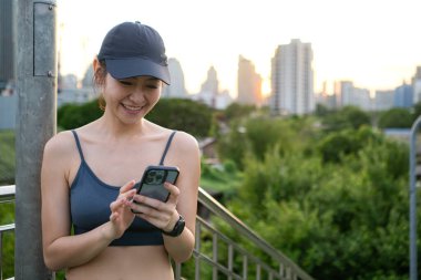 Genç bir kadın, sosyal medyaya bağlanmak ve rahatlatıcı müzik dinlemek için akıllı telefon kullanarak egzersiz yaparken ara veriyor.